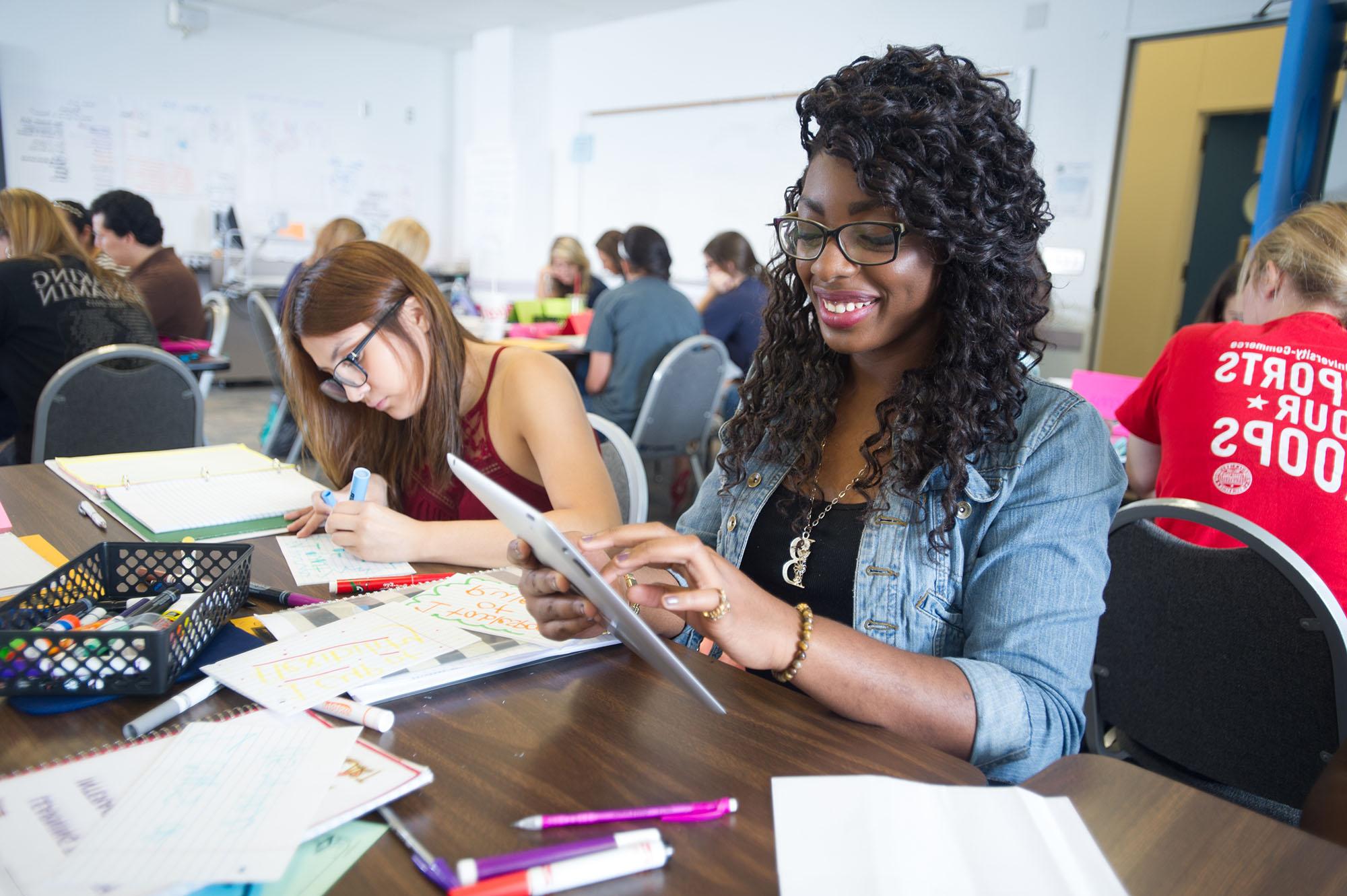 A female student using a tablet for an assignment she is completing with a colleague.