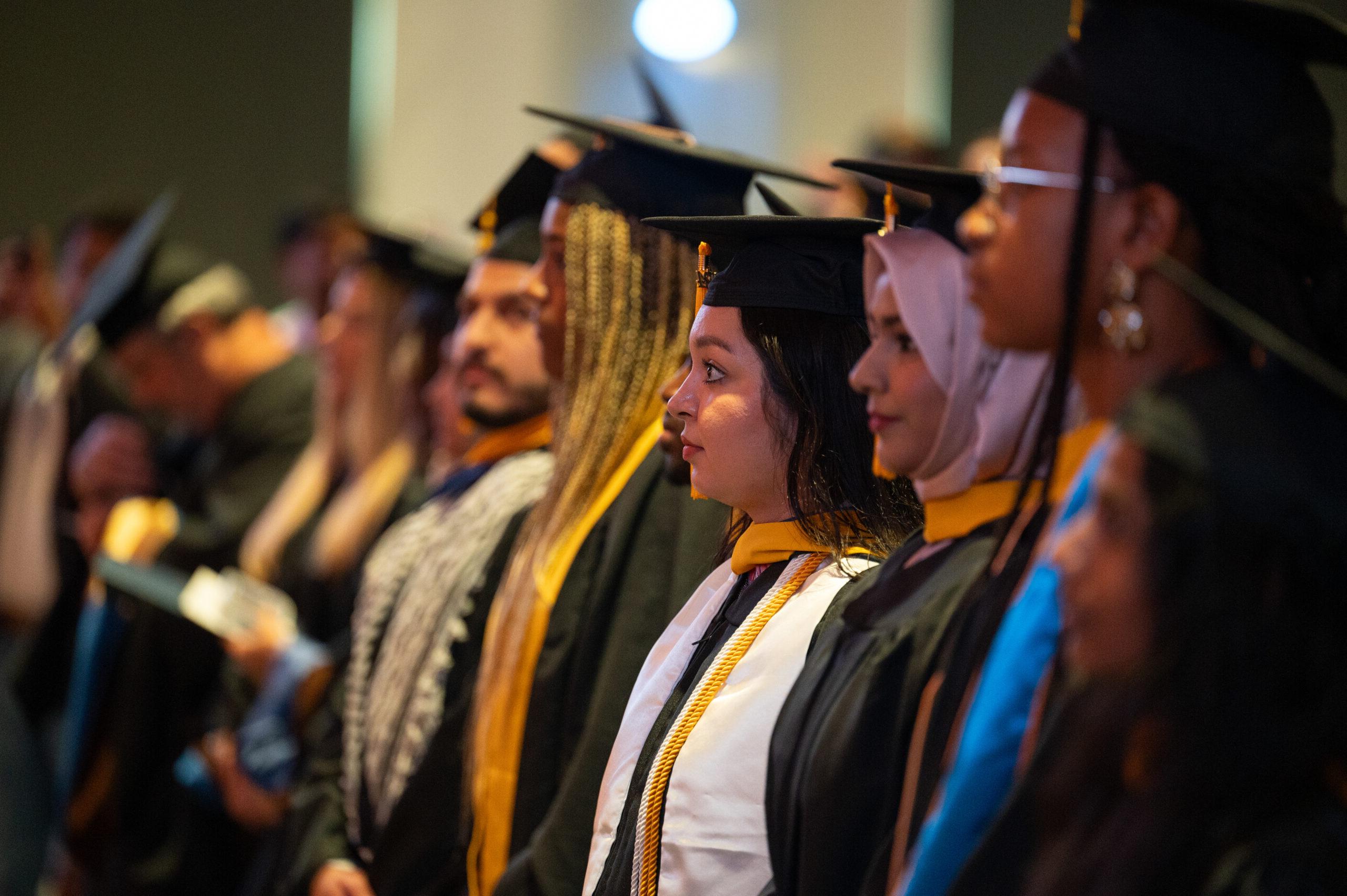 A group of graduate student lined up. There is a focus on a female looking to the right.